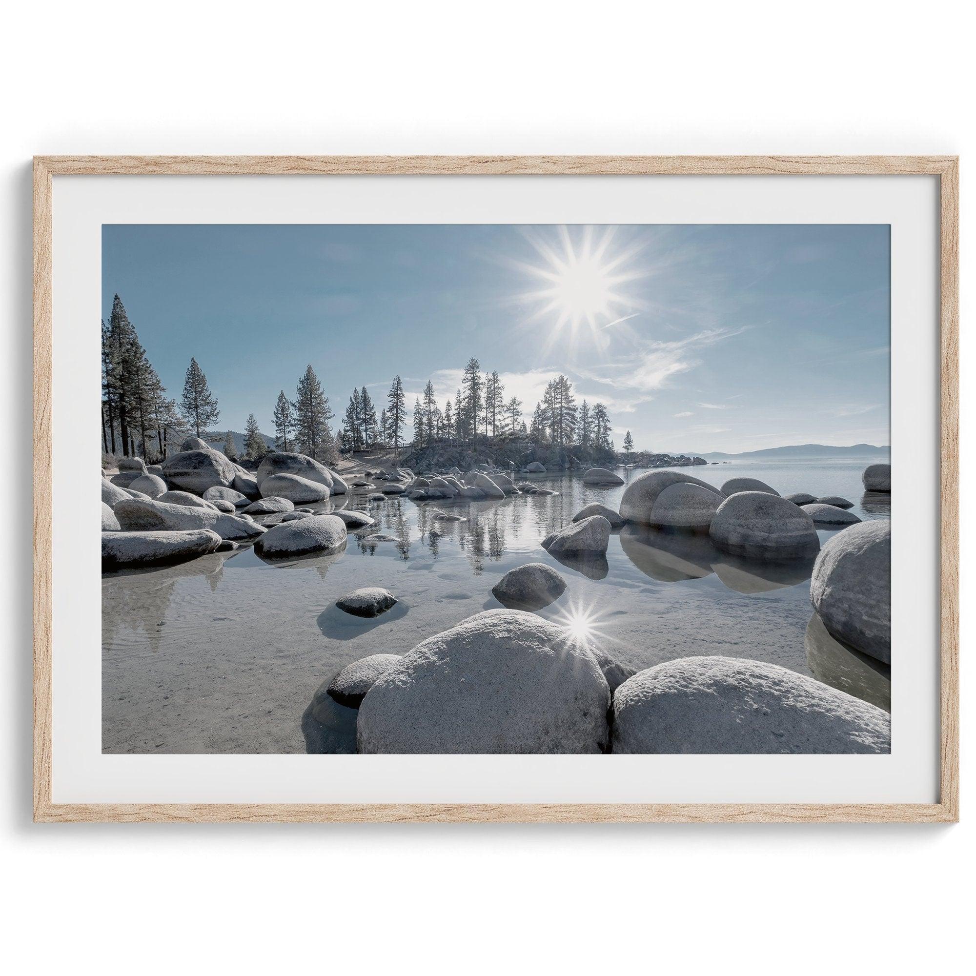 Capture the beauty of Lake Tahoe with this stunning lake wall art. The image showcases majestic rocks rising from crystal-clear water, contrasting with the blue sky. The sun's reflection adds a warm, magical touch to the breathtaking scenery.