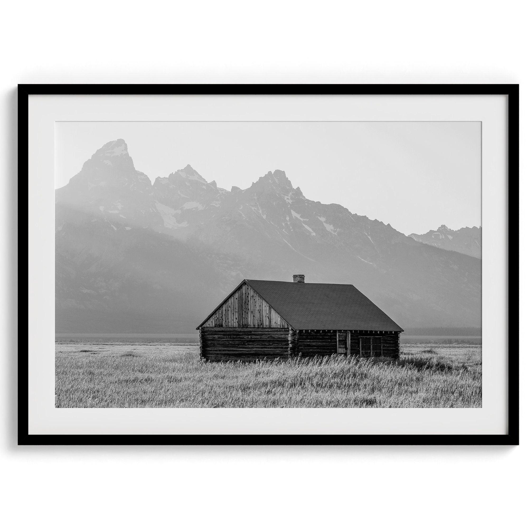 Step into Grand Teton National Park with this fine art black and white mountain print. This western landscape photo showcases a century-old rustic hut at the foot of the snowy, pointy Teton mountains.