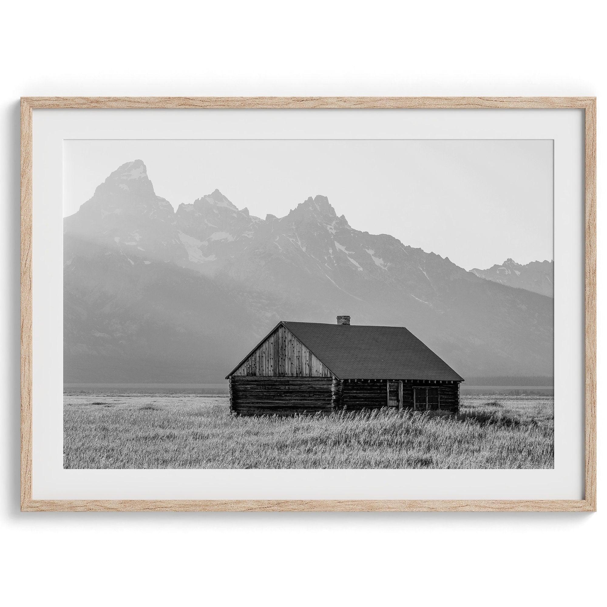 Step into Grand Teton National Park with this fine art black and white mountain print. This western landscape photo showcases a century-old rustic hut at the foot of the snowy, pointy Teton mountains.