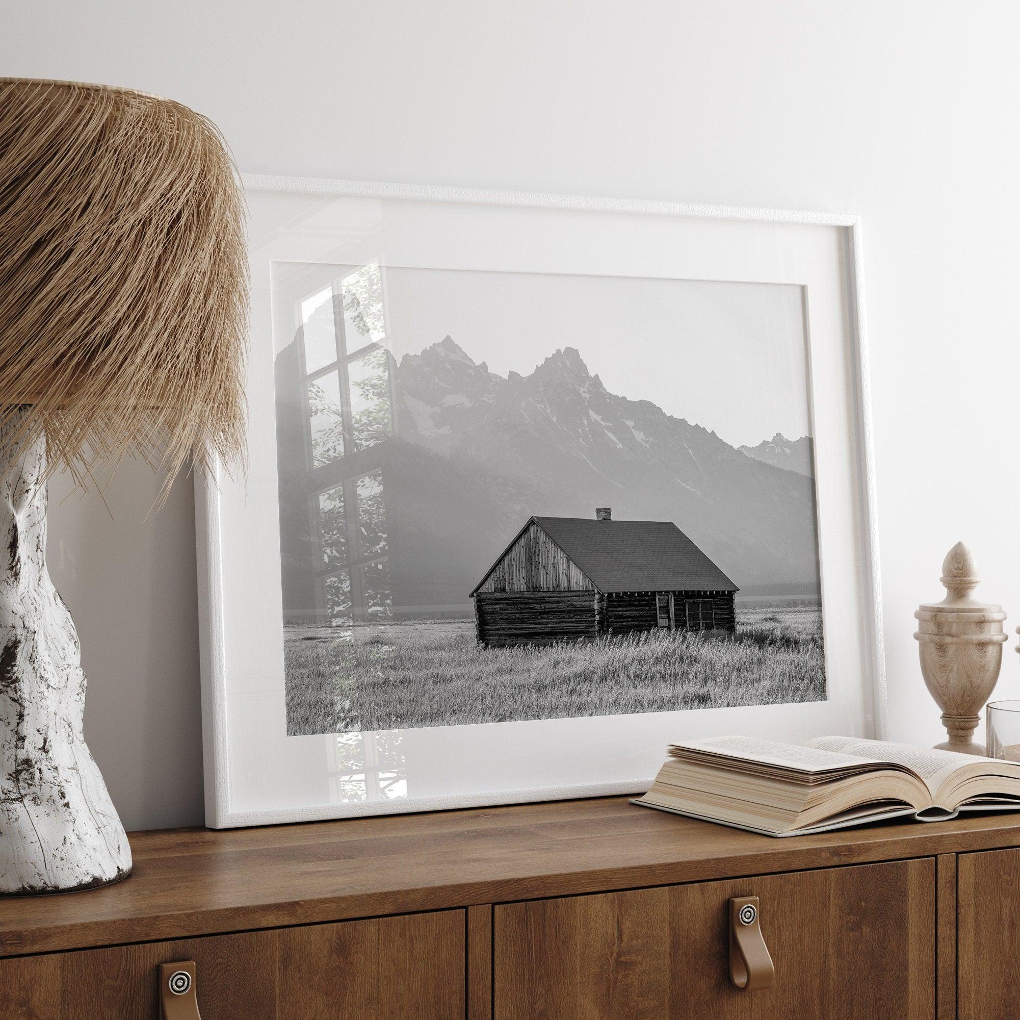 Step into Grand Teton National Park with this fine art black and white mountain print. This western landscape photo showcases a century-old rustic hut at the foot of the snowy, pointy Teton mountains.