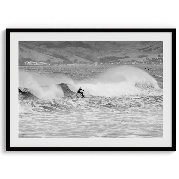 A black and white fine art surf print. This ocean wall art showcases a lone surfer riding the waves in Pismo Beach, California.