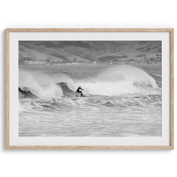 A black and white fine art surf print. This ocean wall art showcases a lone surfer riding the waves in Pismo Beach, California.