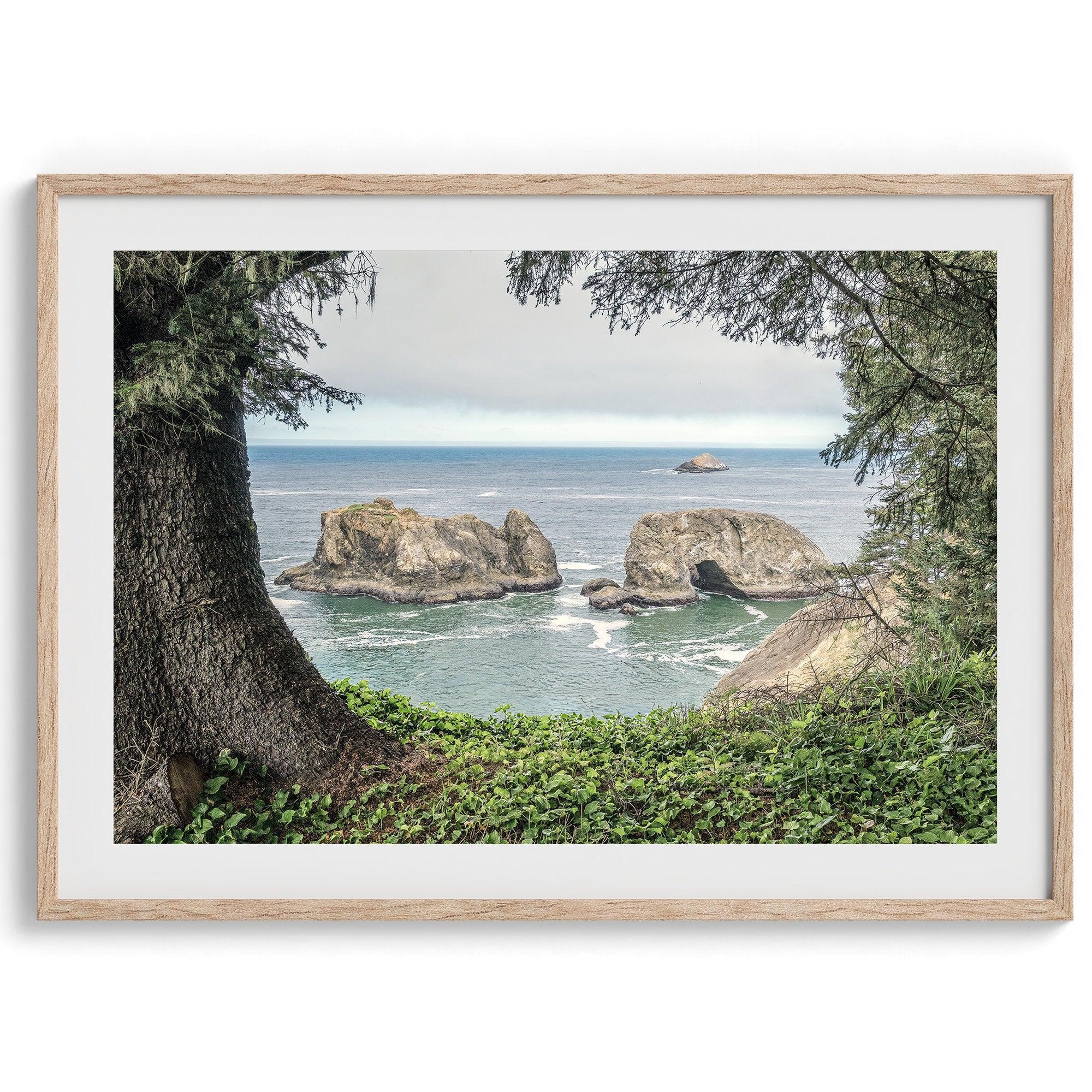 This stunning coastal photo was taken in Samuel H. Boardman State Scenic Corridor in Oregon. This ocean wall art shows unique rock formations in a vast blue Pacific Ocean through a window created from coastal trees and plants.