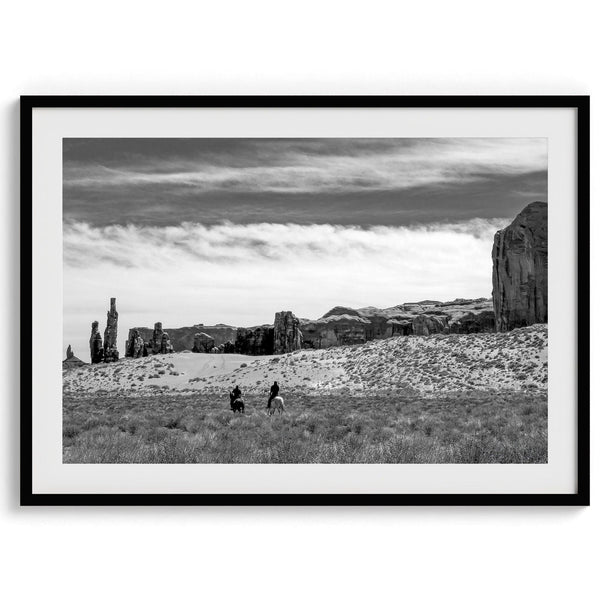 This Utah desert fine art photography print features two horse riders riding toward the horizon of the Utah desert with the unique towering rocks of Monument Valley as the backdrop. The dramatic cloudy sky adds intensity and beauty to the scene.
