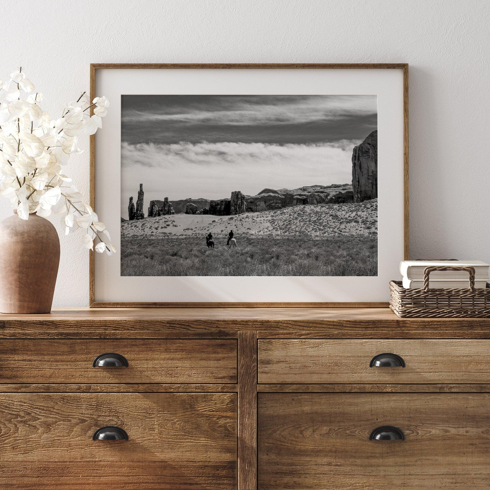 This Utah desert fine art photography print features two horse riders riding toward the horizon of the Utah desert with the unique towering rocks of Monument Valley as the backdrop. The dramatic cloudy sky adds intensity and beauty to the scene.