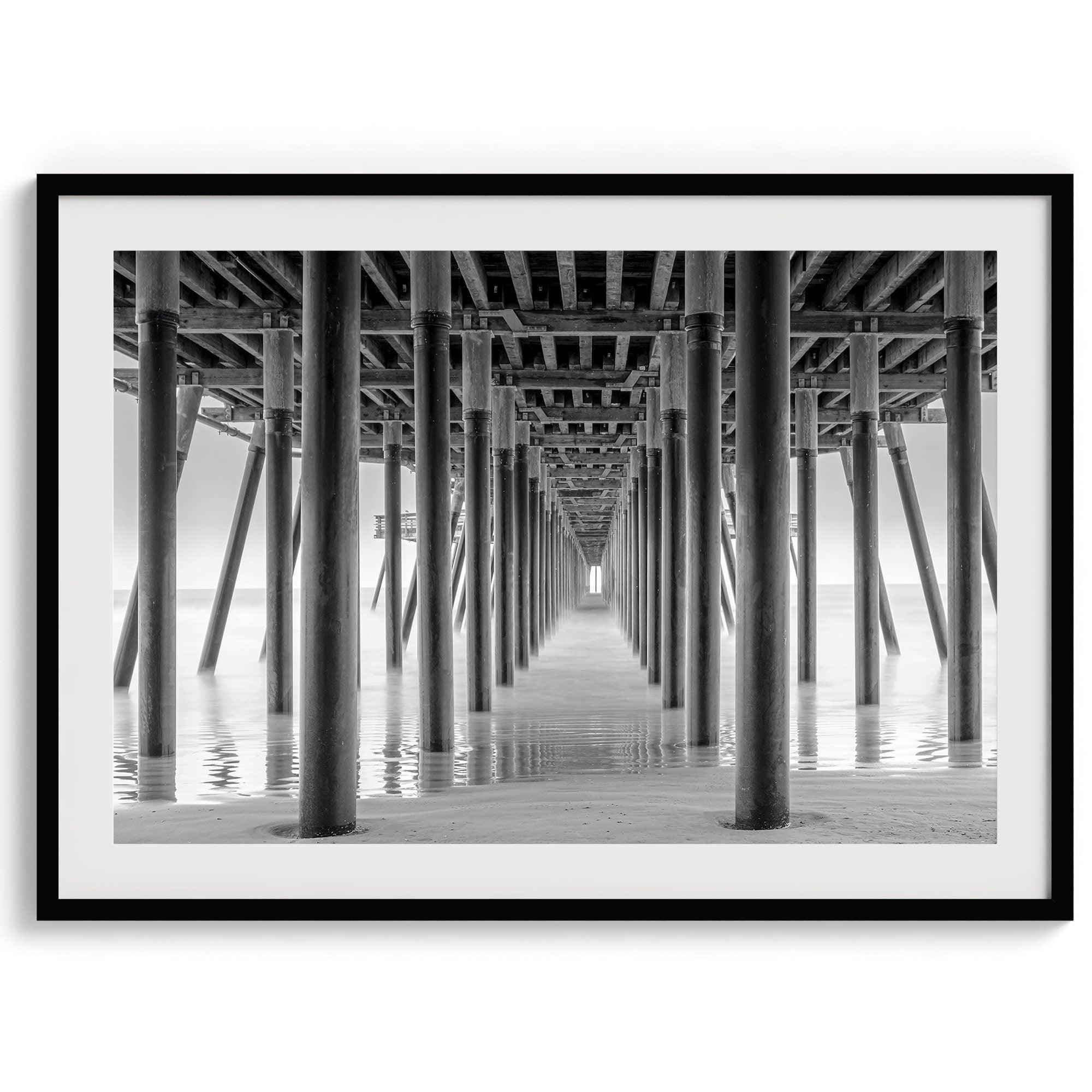 A large fine art abstract black and white beach pier print This stunning beach wall art shows the symmetric structure of the pier with the ocean water gently caressing the pier and beach.