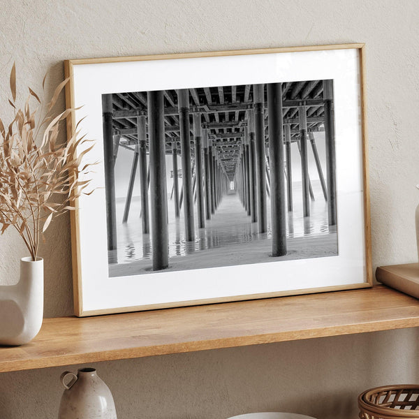 A large fine art abstract black and white beach pier print This stunning beach wall art shows the symmetric structure of the pier with the ocean water gently caressing the pier and beach.