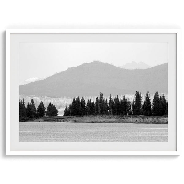 A black and white fine art print of a stunning forest island in the middle of Yellowstone Lake with towering faded mountains in the backdrop