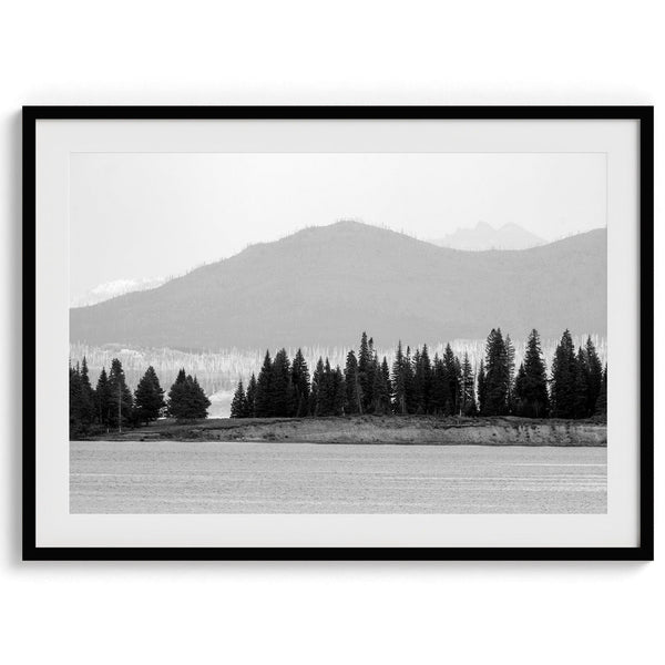 A black and white fine art print of a stunning forest island in the middle of Yellowstone Lake with towering faded mountains in the backdrop