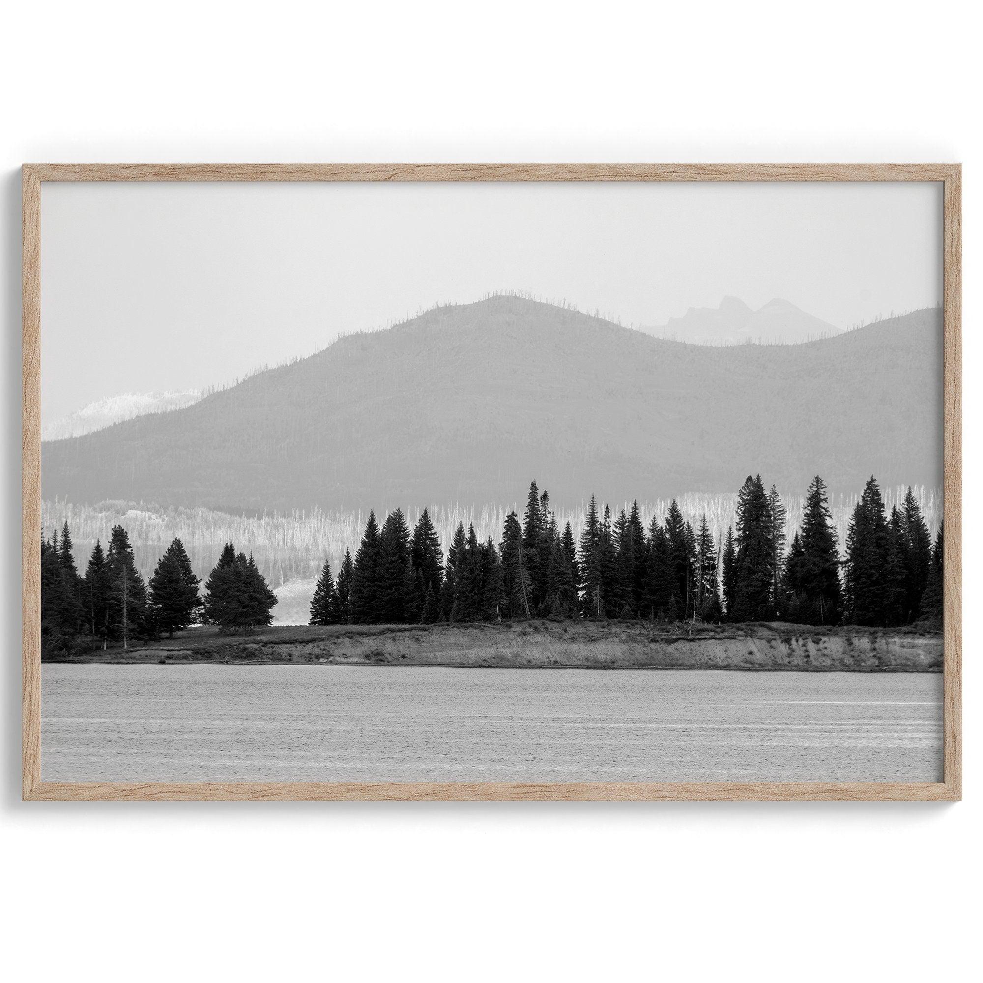 A black and white fine art print of a stunning forest island in the middle of Yellowstone Lake with towering faded mountains in the backdrop