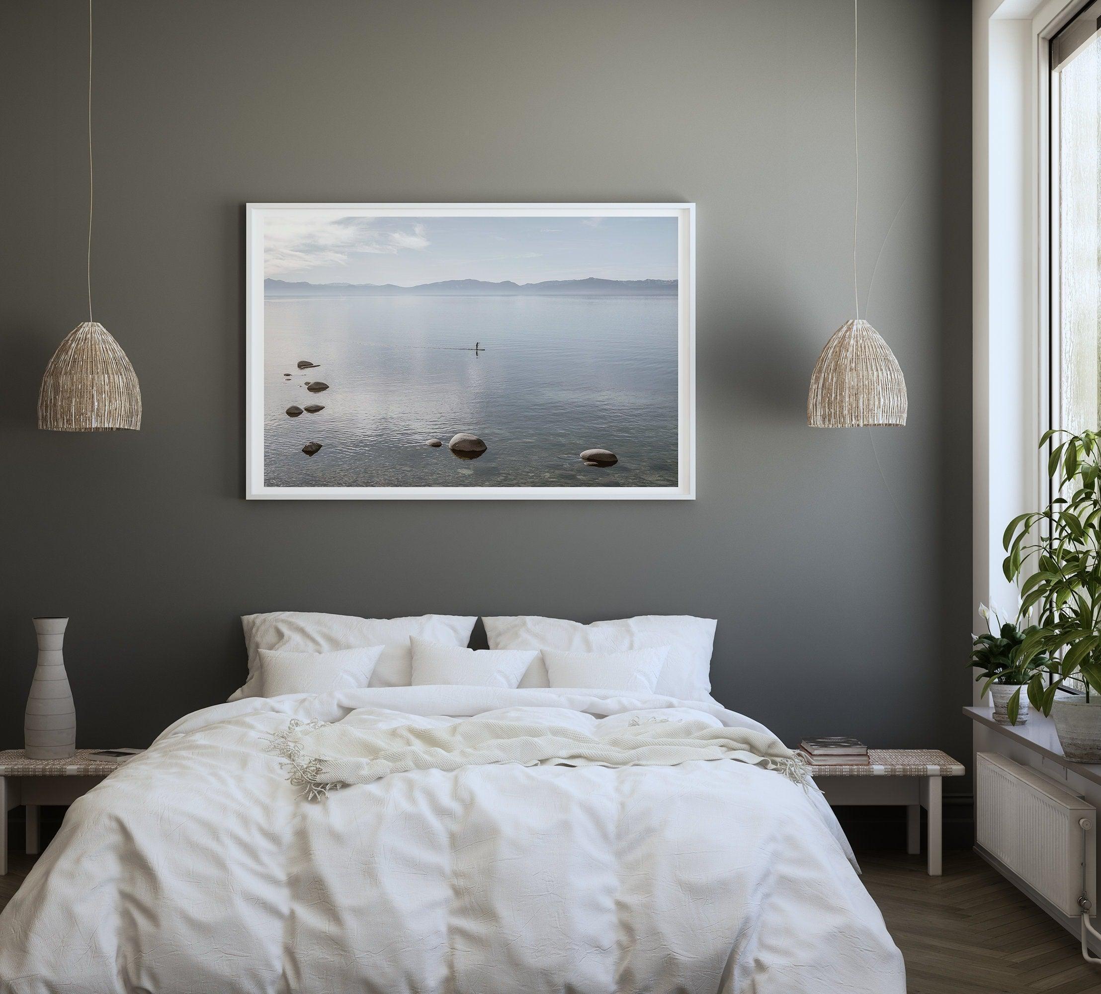 Fine art photography print of Lake Tahoe featuring a serene blue water surrounded by Pacific Northwest mountains, with a lone stand-up paddle silhouette on the lake.