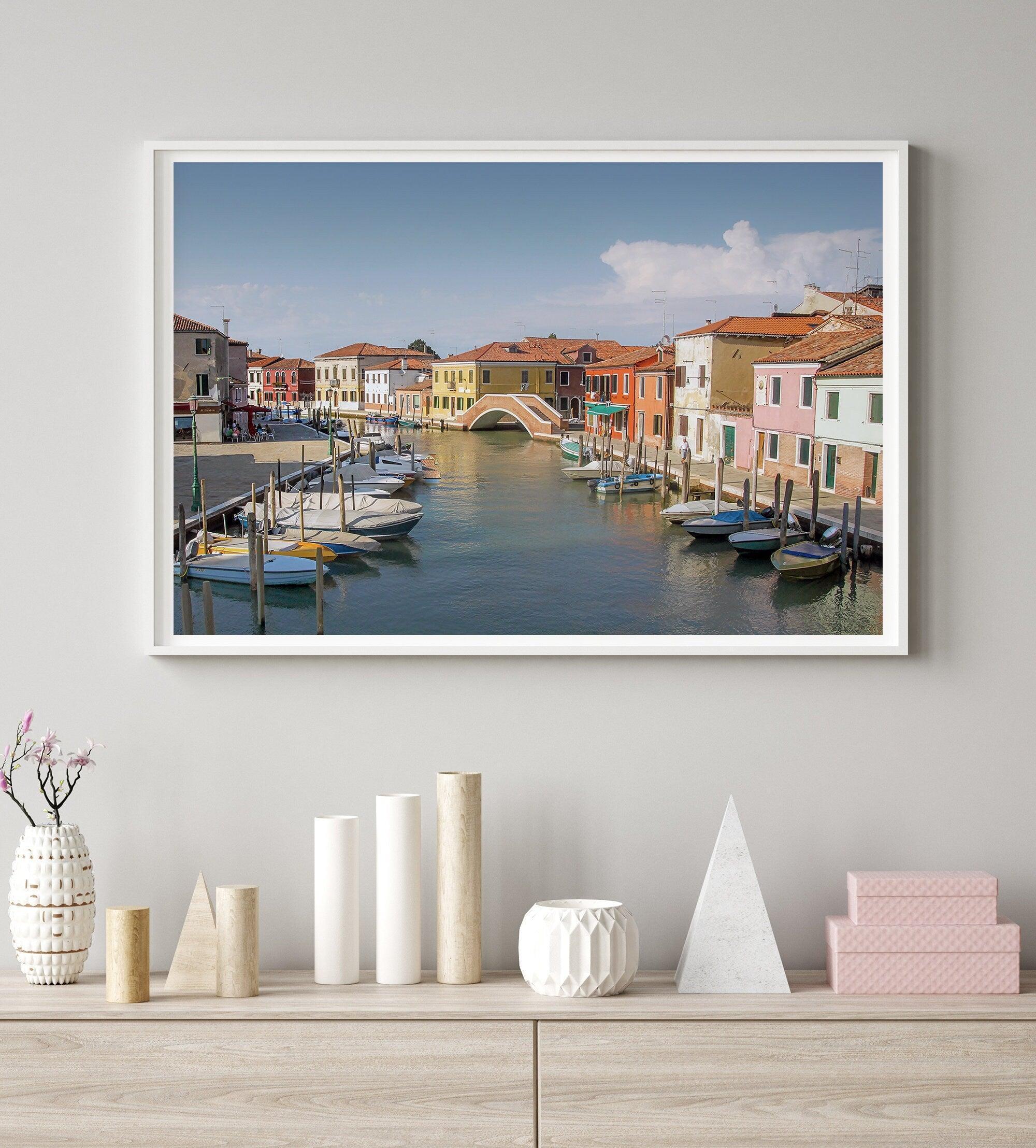 A stunning framed Venice print. The picturesque vibrant streets of Murano are lined with houses in an array of vibrant colors. The sun casts a beautiful glow on the tranquil canal, which adds to the charm of this peaceful Italian town.