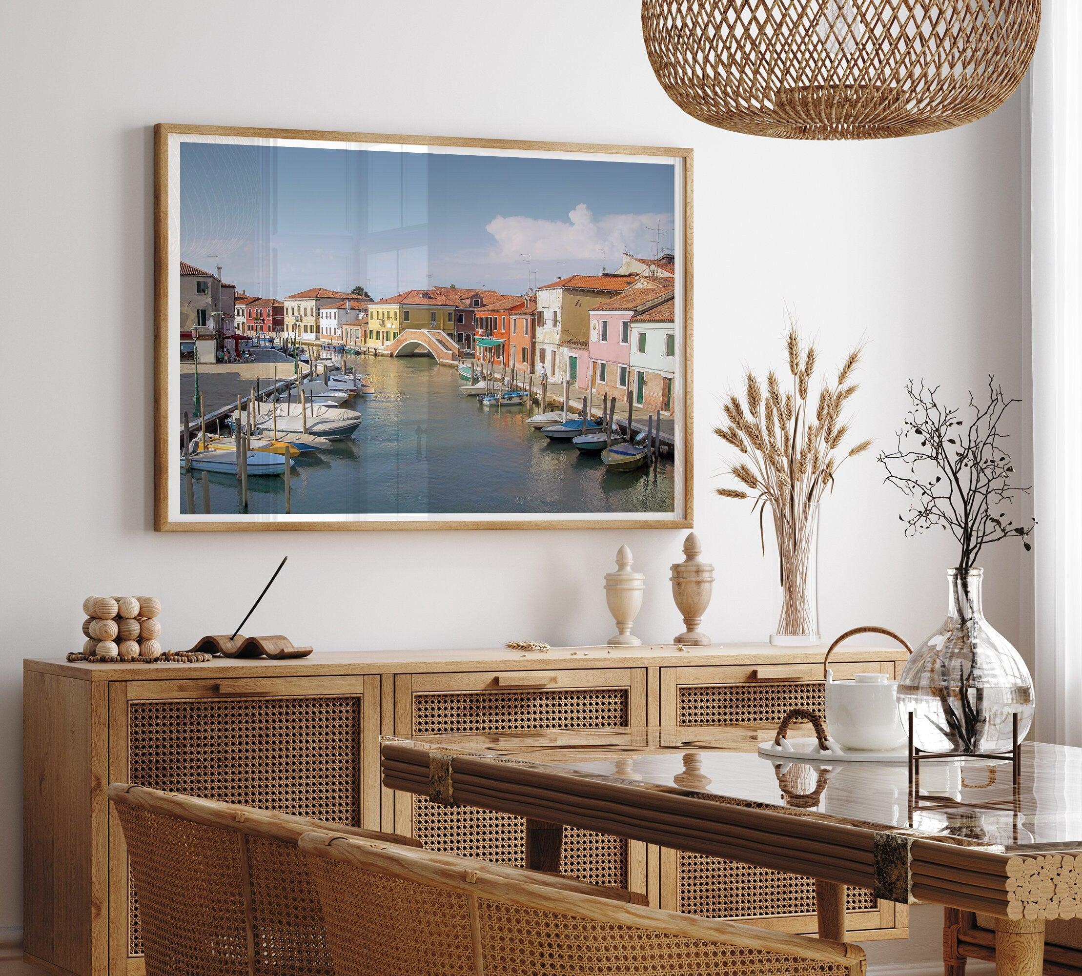 A stunning framed Venice print. The picturesque vibrant streets of Murano are lined with houses in an array of vibrant colors. The sun casts a beautiful glow on the tranquil canal, which adds to the charm of this peaceful Italian town.