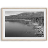 A fine art black and white Lake Tahoe print showcasing docks and boats nested on the lake waters on the left, while the beachfront, nestled against a backdrop of a lush forest and majestic mountain, paints a picturesque scene on the right.