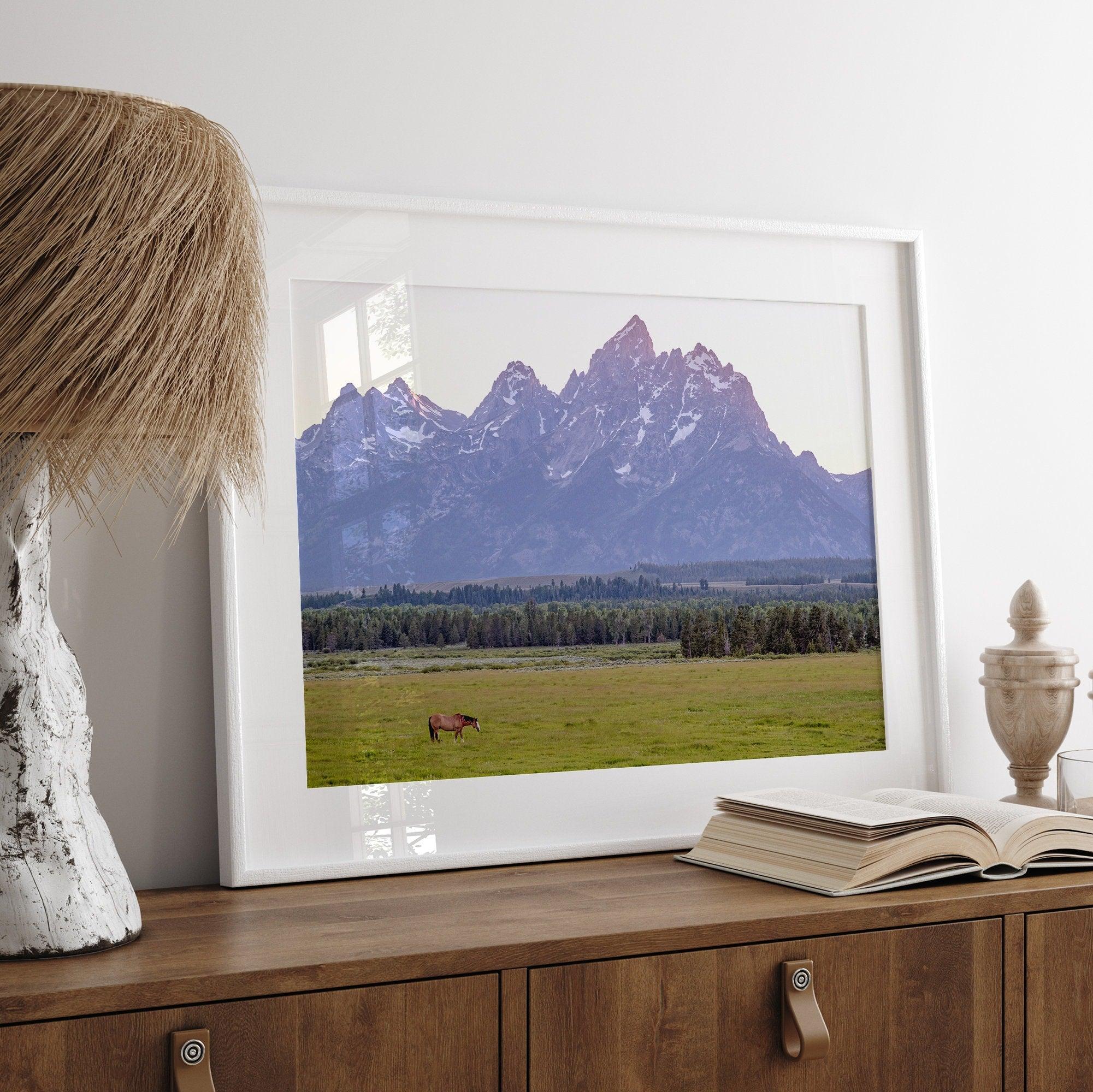 A stunning snow-covered mountain framed or unframed print from Grand Teton National Park with a beautiful horse grazing the grass in the forefront.