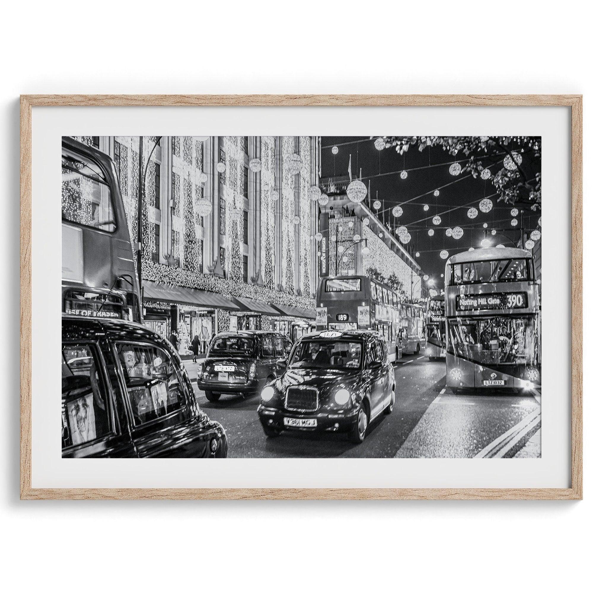 A fine art black and white photography print of a vibrant street in London during the Christmas holidays. This London wall art shows double-decker buses and black taxis, and the streets are adorned with bright holiday lights and festive decorations