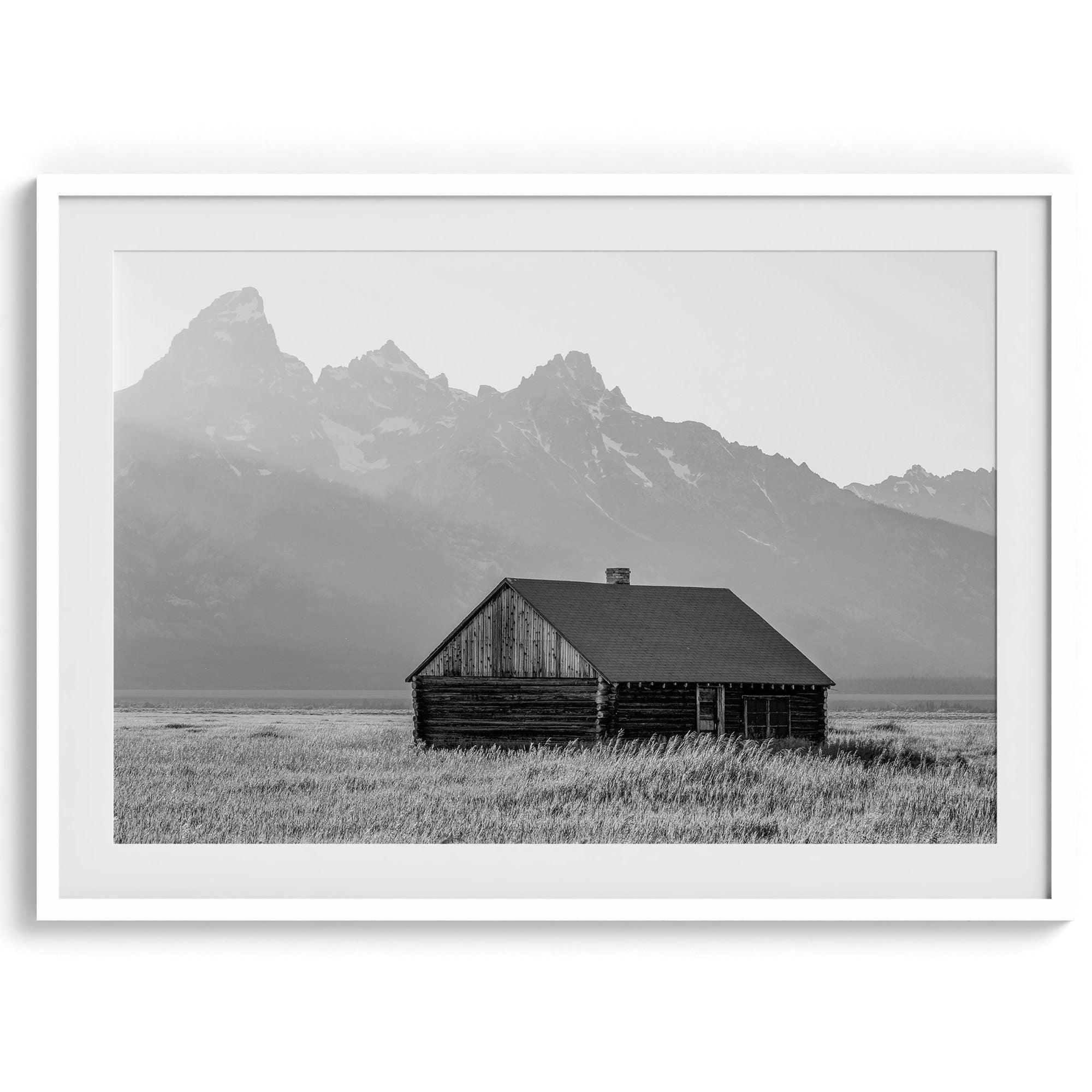 Step into Grand Teton National Park with this fine art black and white mountain print. This western landscape photo showcases a century-old rustic hut at the foot of the snowy, pointy Teton mountains.