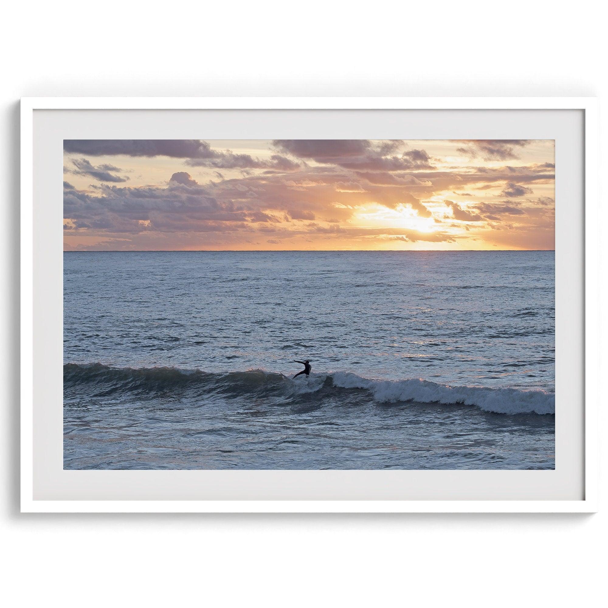 A fine art ocean sunset print showcasing a serene sunset and a lone surfer riding the waves. Taken in Montana De Oro State Park, California.