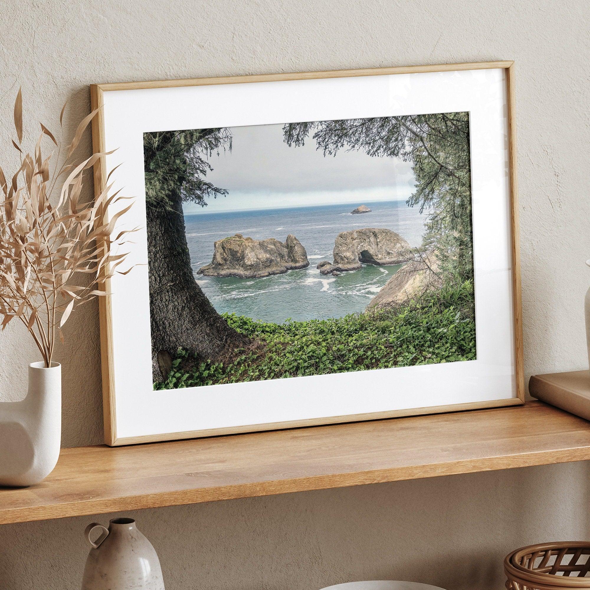 This stunning coastal photo was taken in Samuel H. Boardman State Scenic Corridor in Oregon. This ocean wall art shows unique rock formations in a vast blue Pacific Ocean through a window created from coastal trees and plants.