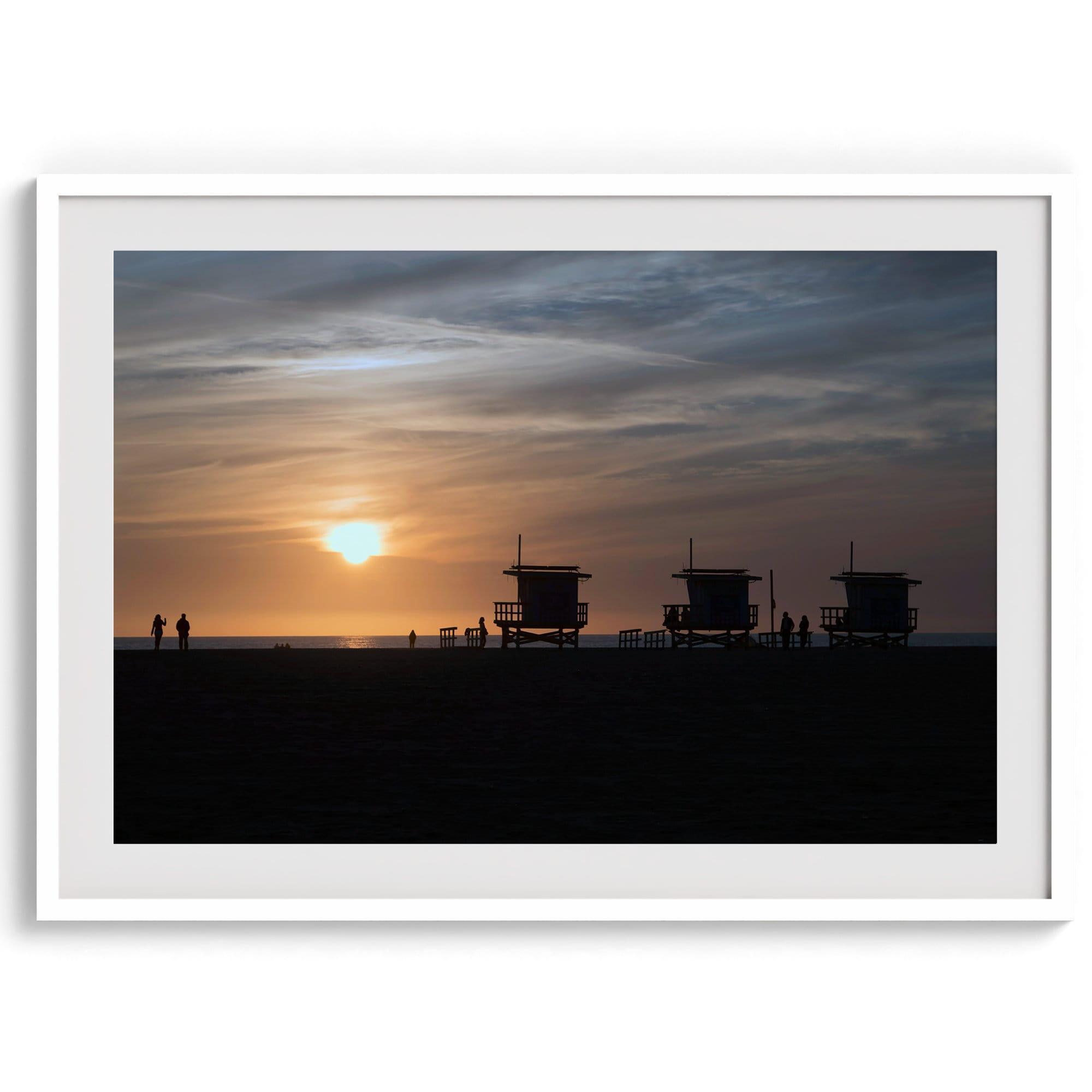 Step into Venice Beach with our fine art beach sunset framed or unframed print. The print showcases the beach in sunset with the silhouettes of the famous lifeguard towers and people in the sunset.