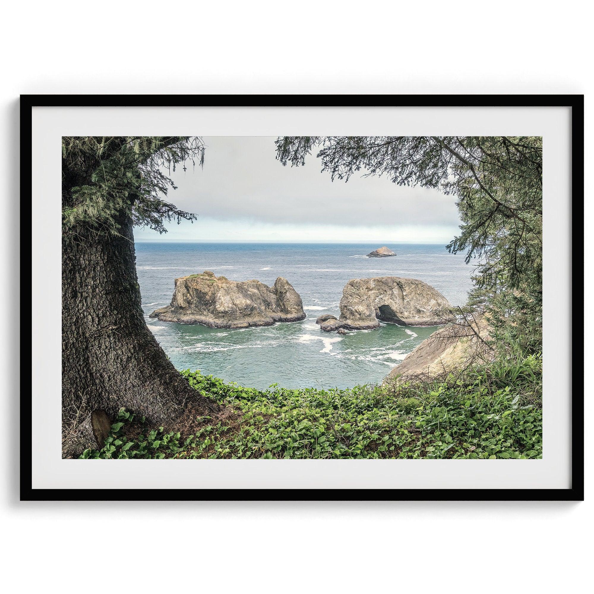 This stunning coastal photo was taken in Samuel H. Boardman State Scenic Corridor in Oregon. This ocean wall art shows unique rock formations in a vast blue Pacific Ocean through a window created from coastal trees and plants.