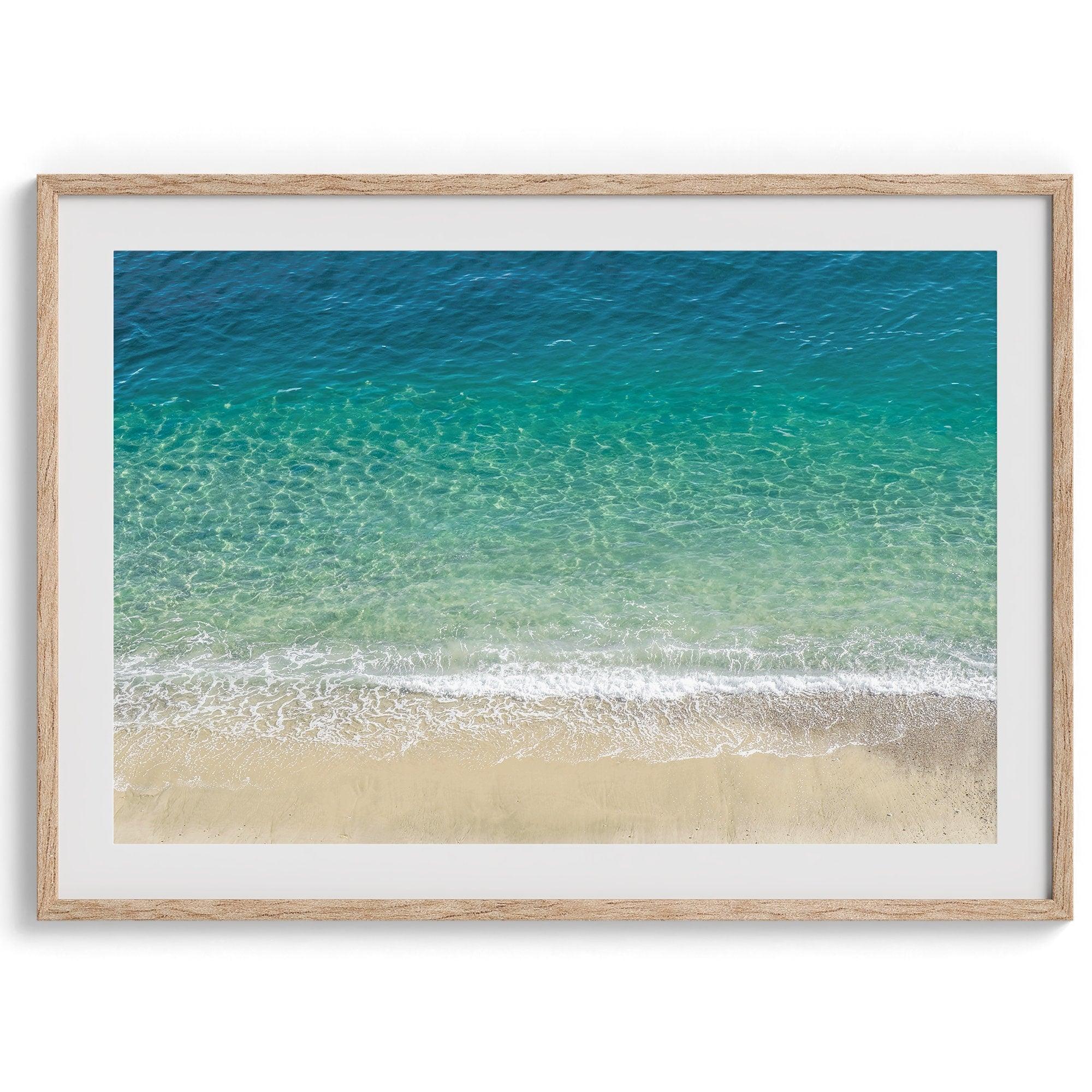 This fine art aerial beach print showcases the mesmerizing colors of the ocean in vivid detail. From the deep blue depths to the vibrant greenish turquoise blue, transitioning to the golden sandy beach and the crashing white surf.