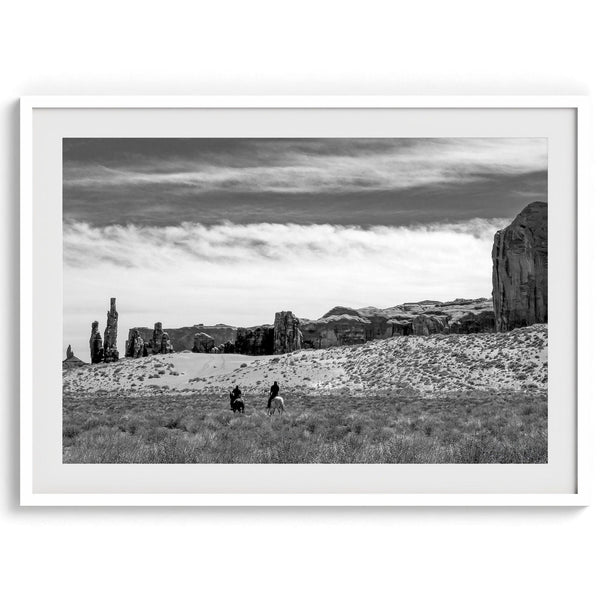 This Utah desert fine art photography print features two horse riders riding toward the horizon of the Utah desert with the unique towering rocks of Monument Valley as the backdrop. The dramatic cloudy sky adds intensity and beauty to the scene.