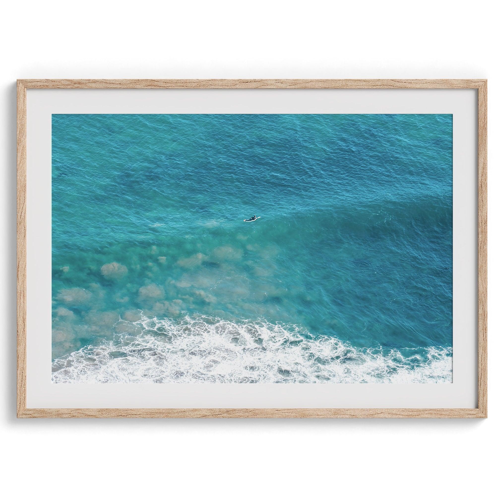 A fine art ocean print of an aerial beach showing a lone surfer with a large wave underneath.