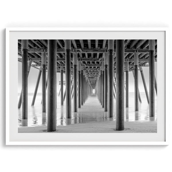 A large fine art abstract black and white beach pier print This stunning beach wall art shows the symmetric structure of the pier with the ocean water gently caressing the pier and beach.