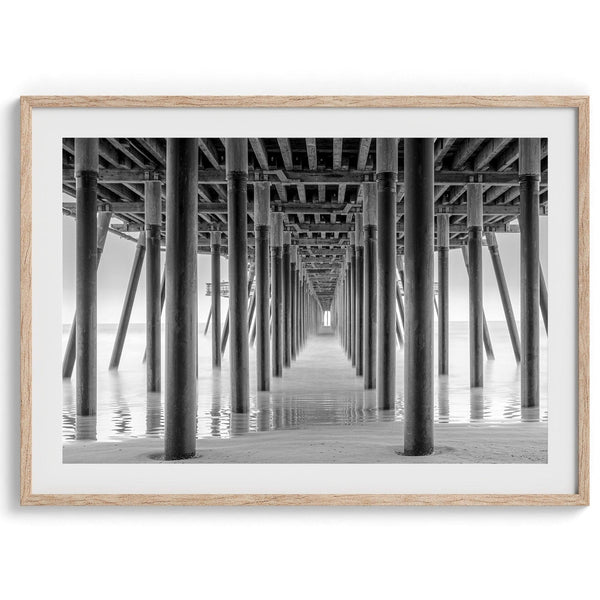 A large fine art abstract black and white beach pier print This stunning beach wall art shows the symmetric structure of the pier with the ocean water gently caressing the pier and beach.