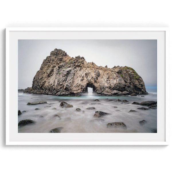 Fine art print showcasing a magnificent rock formation framing the horizon and crashing waves, with scattered rocks adding texture. Captivating and soothing, this print is a timeless addition to any space, evoking relaxation and awe-inspiring beauty.