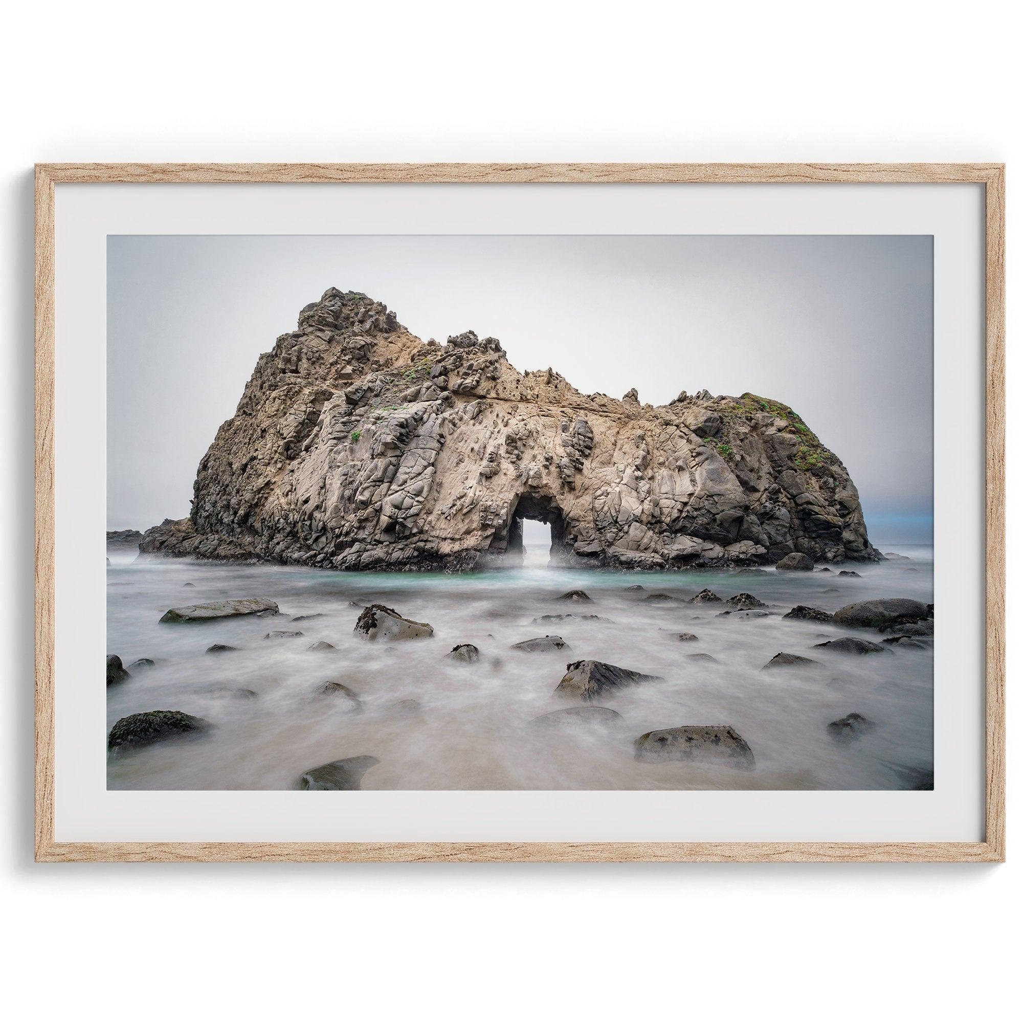 Fine art print showcasing a magnificent rock formation framing the horizon and crashing waves, with scattered rocks adding texture. Captivating and soothing, this print is a timeless addition to any space, evoking relaxation and awe-inspiring beauty.