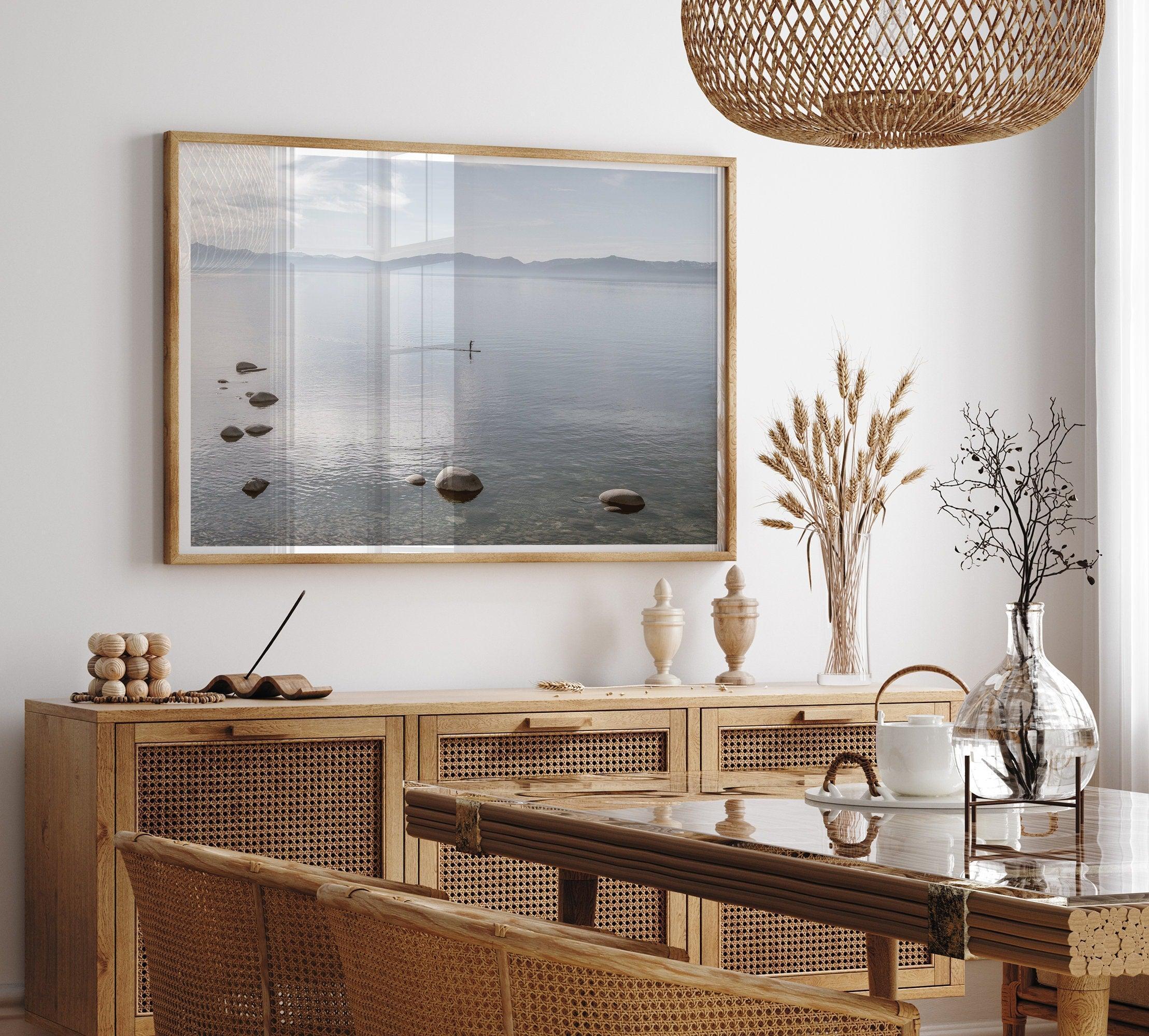 Fine art photography print of Lake Tahoe featuring a serene blue water surrounded by Pacific Northwest mountains, with a lone stand-up paddle silhouette on the lake.