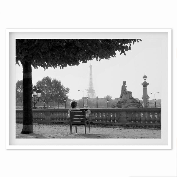 A fine art print of a woman reading a book in a Parisian garden with the backdrop of the Eiffel Tower.