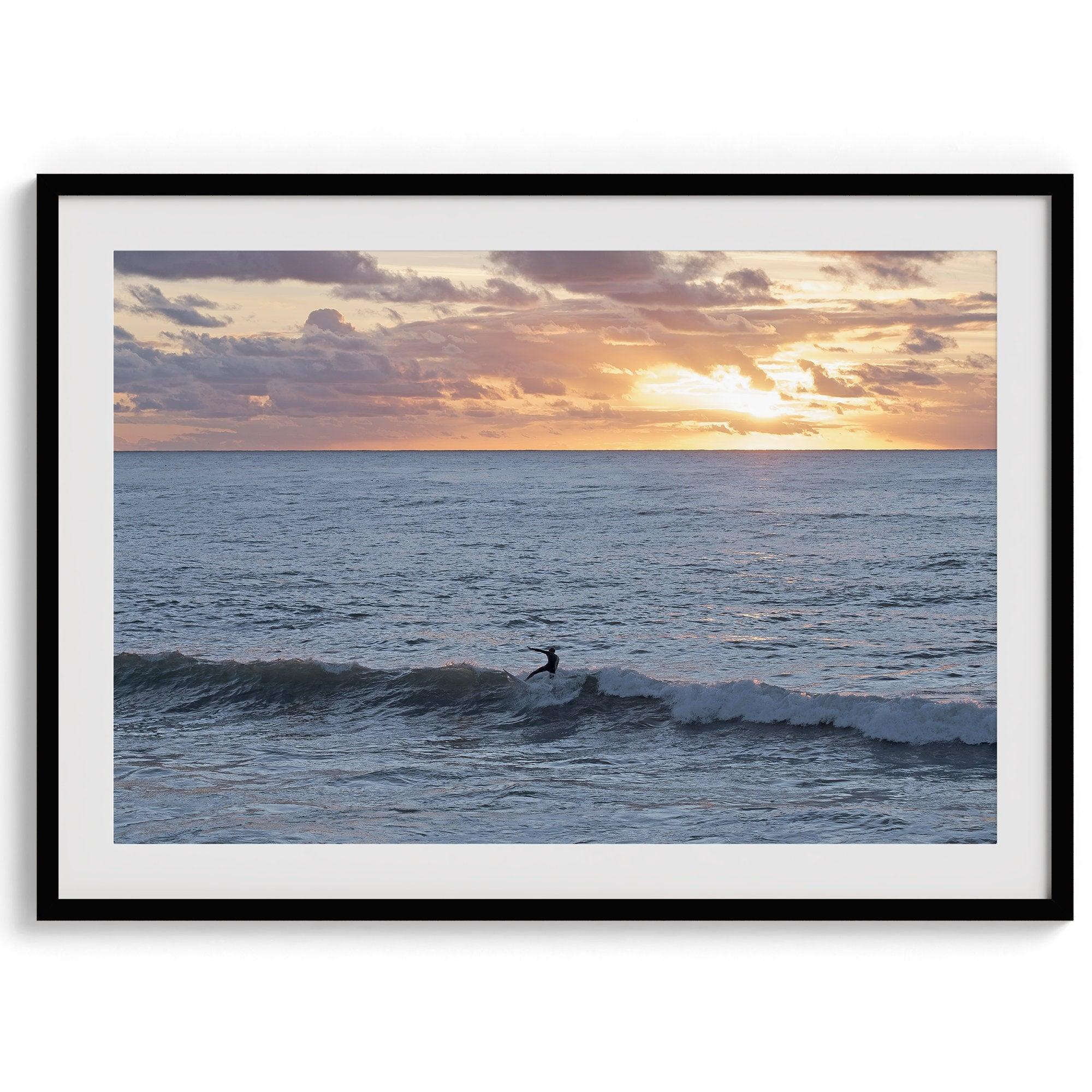 A fine art ocean sunset print showcasing a serene sunset and a lone surfer riding the waves. Taken in Montana De Oro State Park, California.