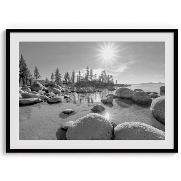 Capture the beauty of Lake Tahoe with this stunning black and white lake wall art. The image showcases majestic rocks rising from crystal-clear water. The reflection of the sun in the water adds a magical touch to the breathtaking scenery.