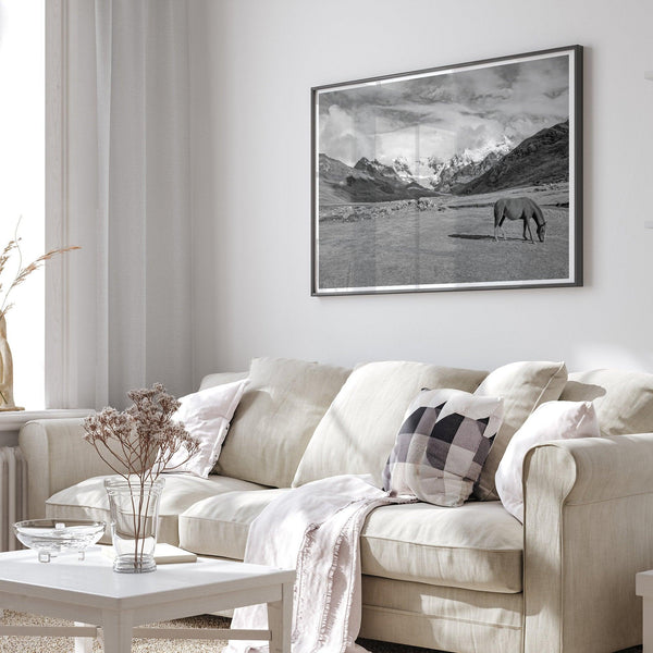 A black and white mountain horse fine art print that can come framed on unframed and was taken in Peru. This mountain wall art showcases snow-covered mountains in Peru and a charming horse grazing relaxingly in the forefront of the picture.
