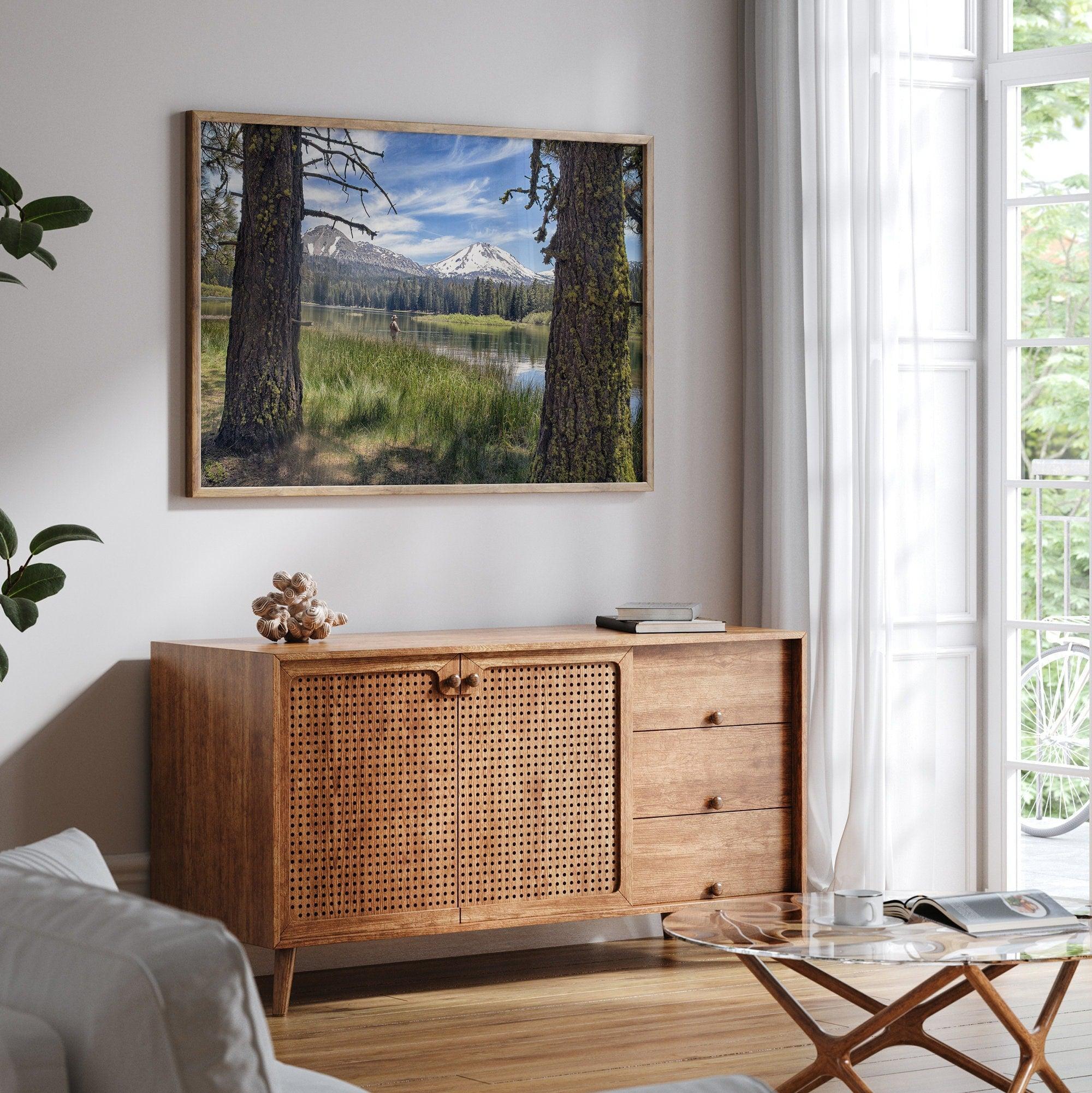 A framed or unframed mountain photo print capturing a fisherman fly fishing in a serene lake, with snow-capped mountains in the backdrop.