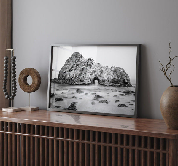 A fine art black and white print of Big Sur Pfeiffer Beach. This beach wall art shows a huge rock on the beach with an opening towards the open sea. This fine art photograph is shot in long exposure so the waves look creamy, gliding over the rocks