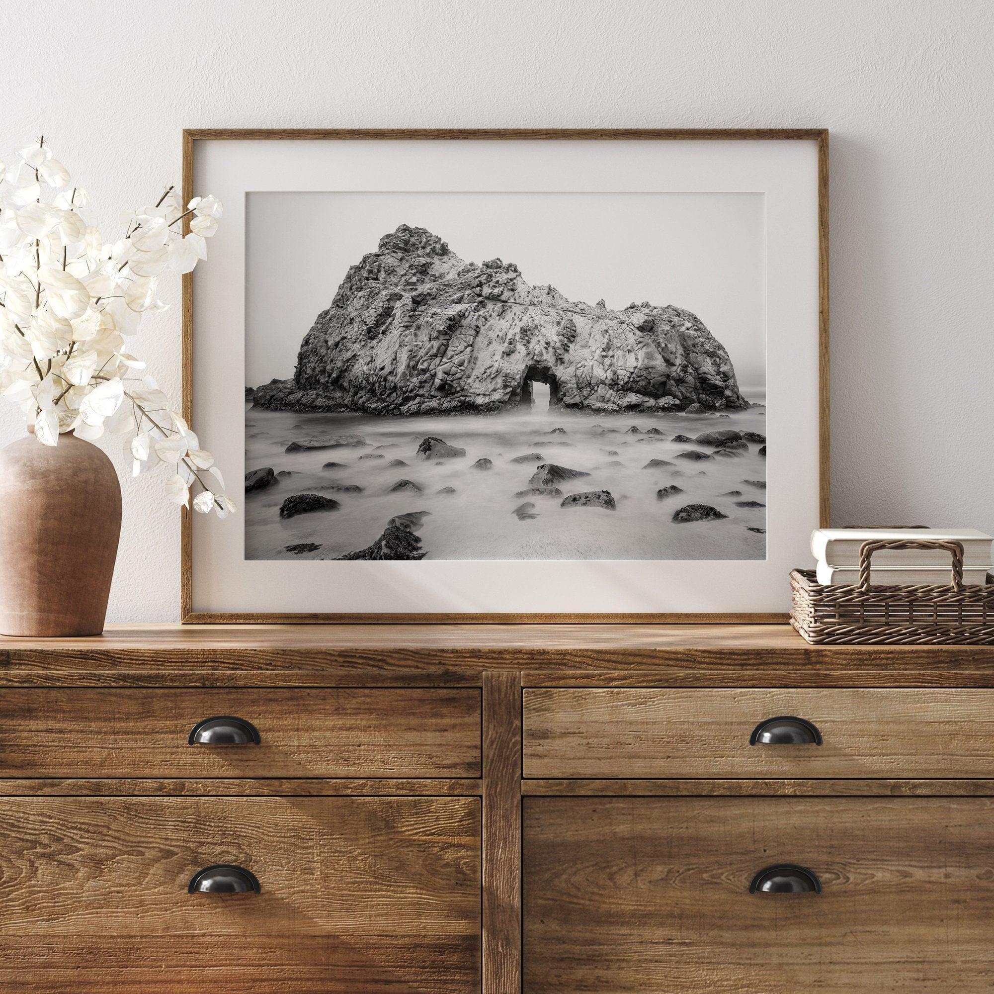 A fine art black and white print of Big Sur Pfeiffer Beach. This beach wall art shows a huge rock on the beach with an opening towards the open sea. This fine art photograph is shot in long exposure so the waves look creamy, gliding over the rocks