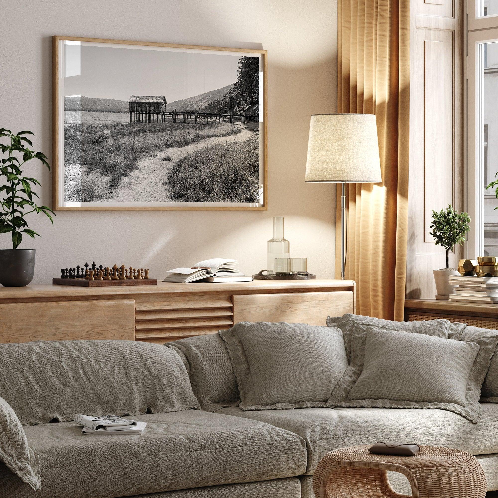 A fine art black and white vintage style framed photography print featuring a rustic old boathouse nested on a Lake Tahoe beach.