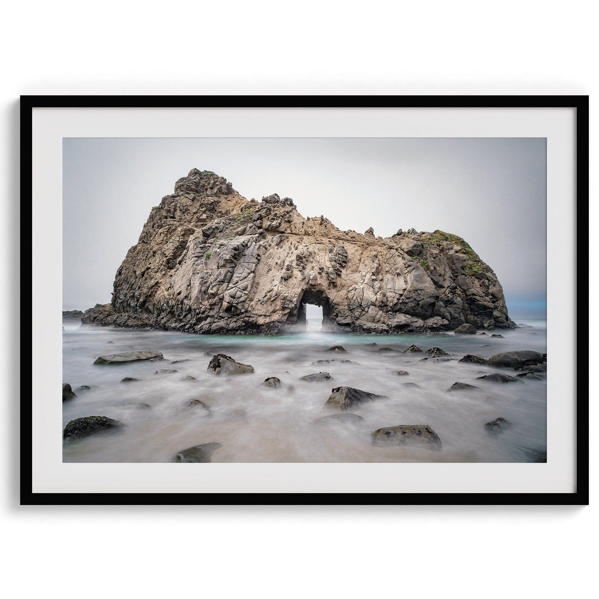 Fine art print showcasing a magnificent rock formation framing the horizon and crashing waves, with scattered rocks adding texture. Captivating and soothing, this print is a timeless addition to any space, evoking relaxation and awe-inspiring beauty.