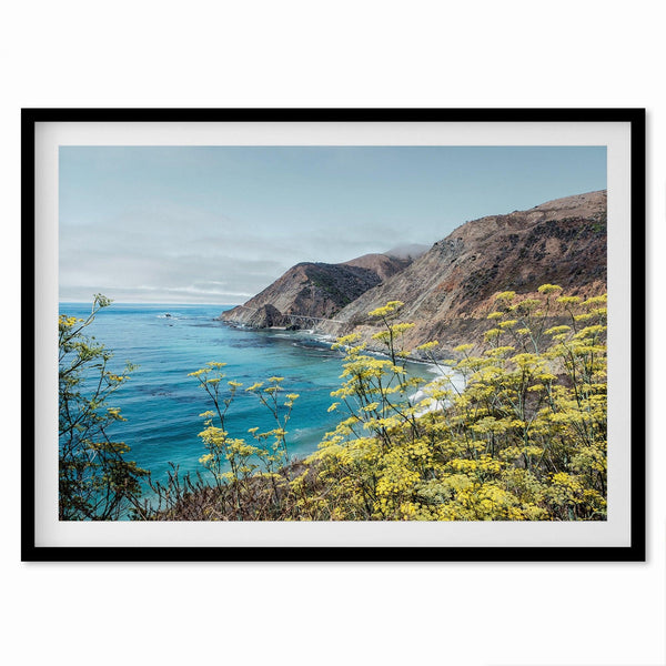 Capture the awe-inspiring coastal beauty with our fine art coastal print. Bixby Bridge spans the cliffs amidst vibrant yellow flowers, complementing the serene blue ocean. Perfect for framed or unframed wall art display.