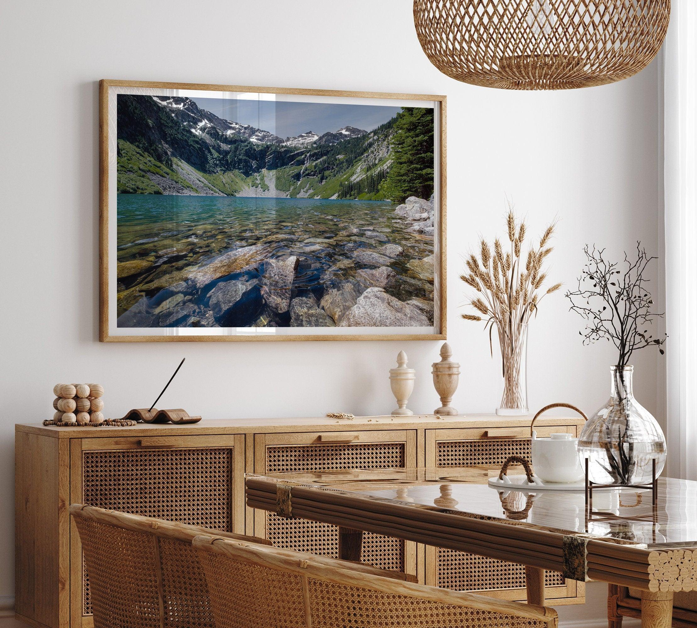 A fine art nature landscape framed print of blue lake in Washington State. The serene lake has vivid colors and clear water. So clear that you can see the stunning rocks at the bottom of the lake. In the backdrop, there are snow-covered mountains.