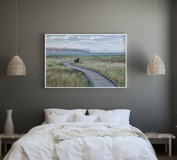 A fine art nature photography print featuring an inspiring winding path through the grassy wilderness of the eastern Sierra Nevada mountains toward Mono Lake. you can see the blue water of the lake in the background and a bench on the road.