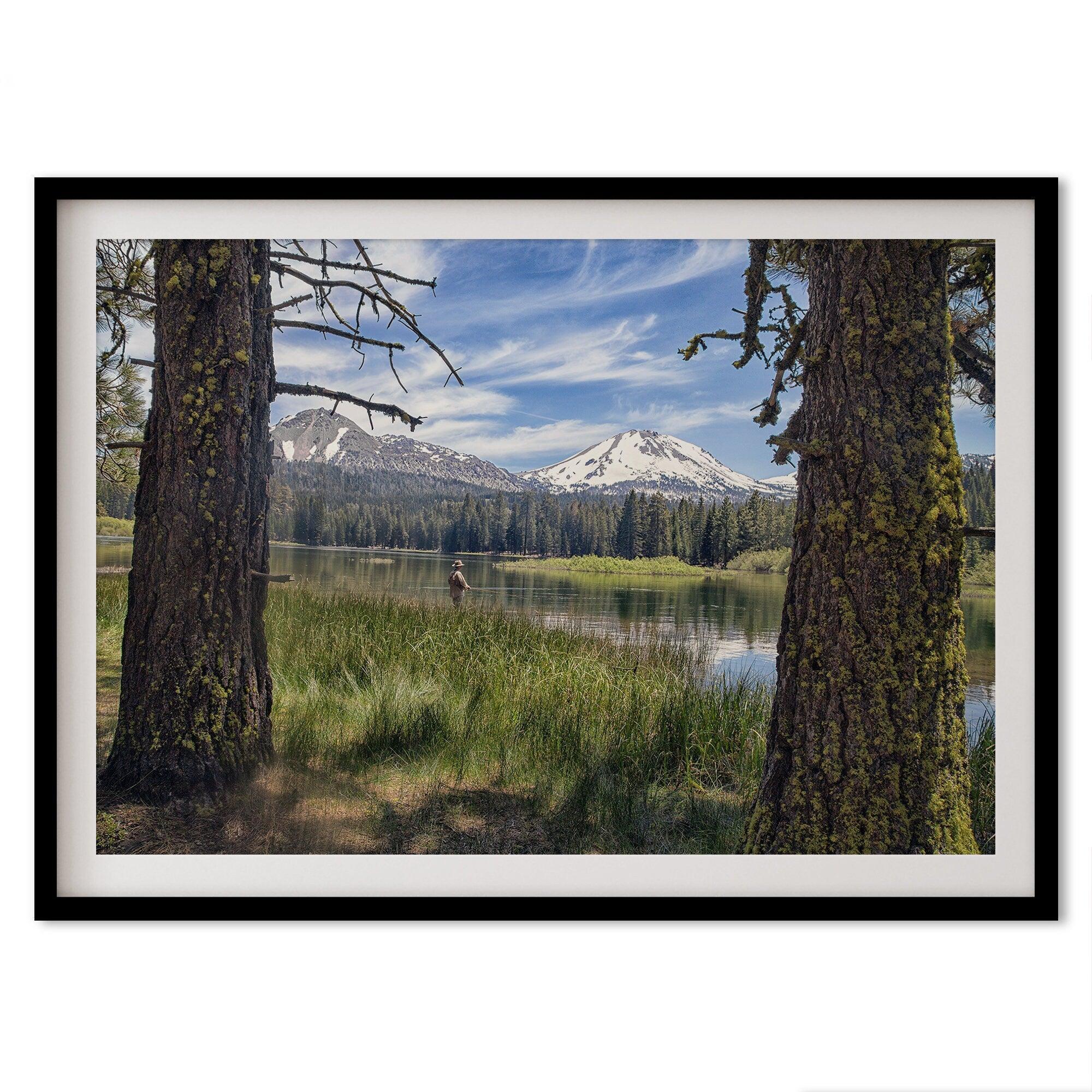 A framed or unframed mountain photo print capturing a fisherman fly fishing in a serene lake, with snow-capped mountains in the backdrop.