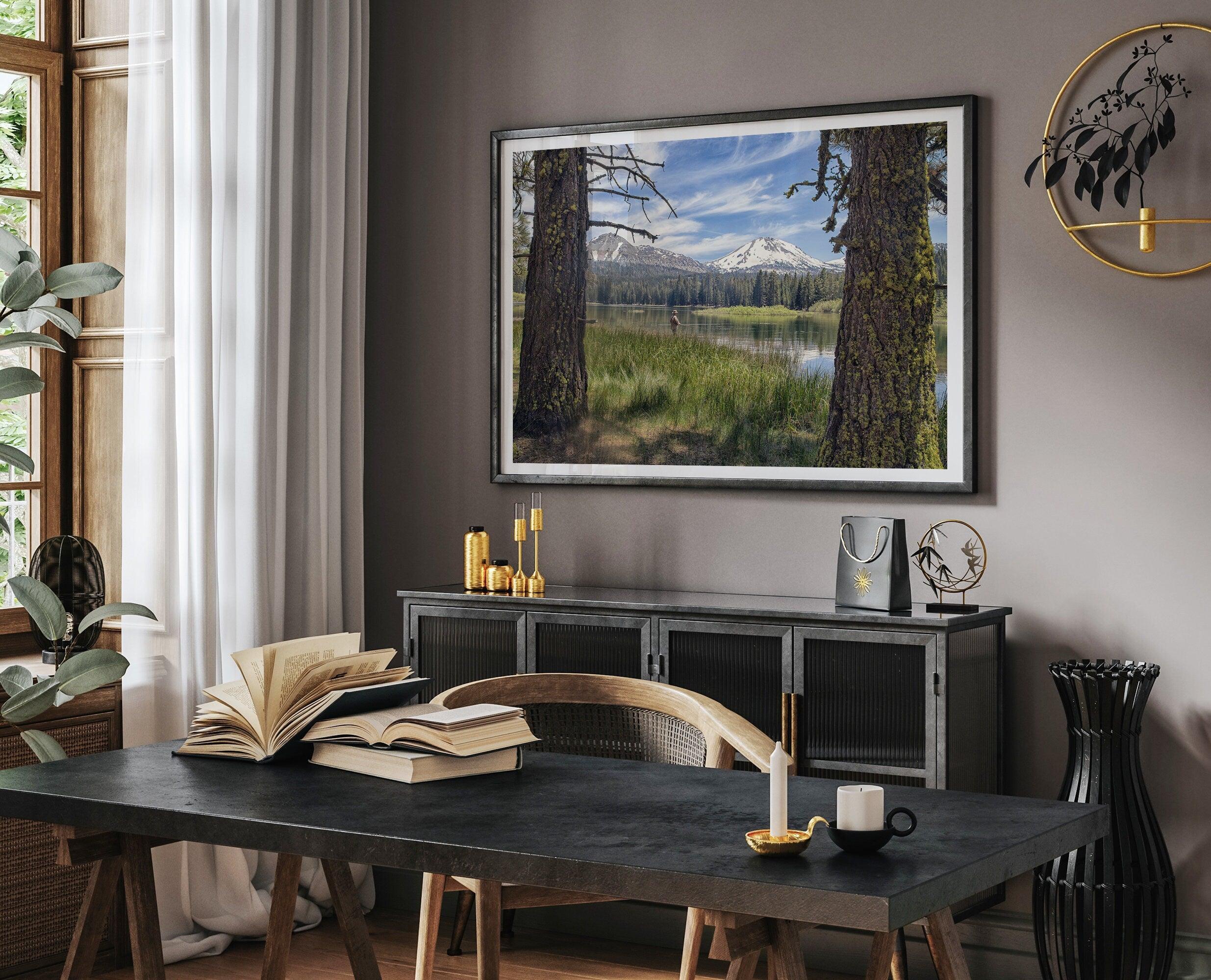 A framed or unframed mountain photo print capturing a fisherman fly fishing in a serene lake, with snow-capped mountains in the backdrop.