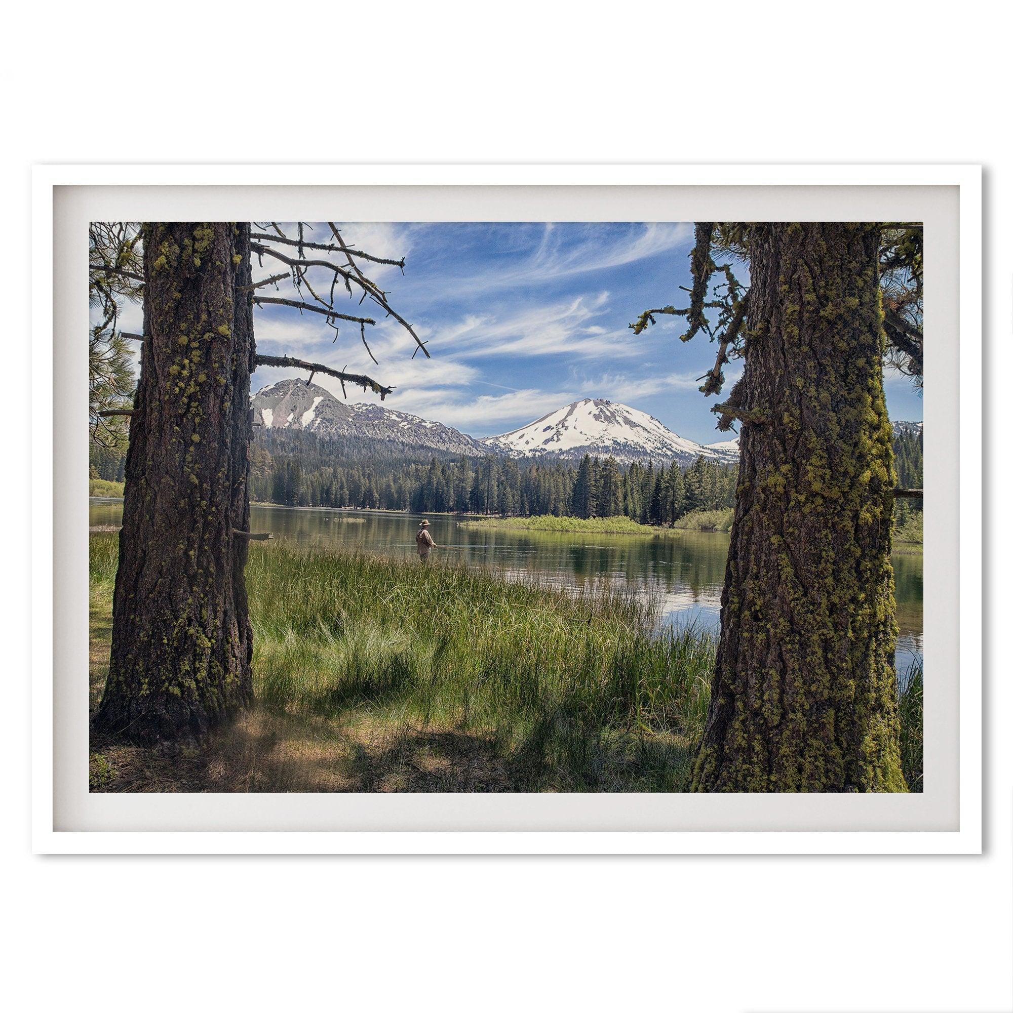 A framed or unframed mountain photo print capturing a fisherman fly fishing in a serene lake, with snow-capped mountains in the backdrop.