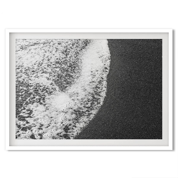 A minimalist fine art black and white beach print showing the ocean surf gently crashing onto a black sand beach in Maui, Hawaii.