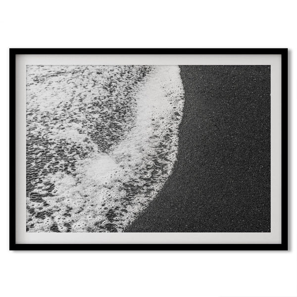 A minimalist fine art black and white beach print showing the ocean surf gently crashing onto a black sand beach in Maui, Hawaii.